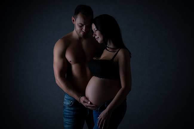 Partner steht neben seiner schwangeren Frau und hät zärtlich ihren Schwangerschaftsbauch